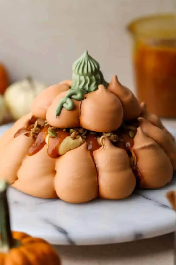 A pumpkin cream pavlova in the shape of a soft pumpkin with a green stem.