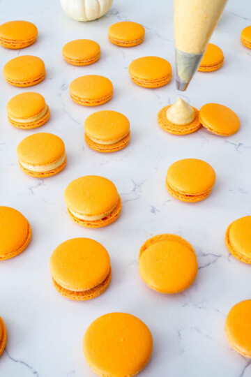 Adding filling to an open macaron, next to several other macrons, both filled and unfilled.