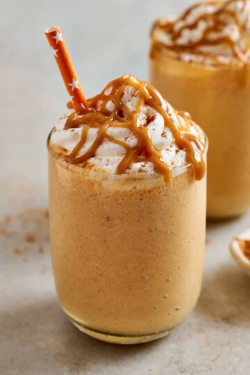 A glass full of pumpkin milkshake topped with a caramel drizzle over whipped cream.