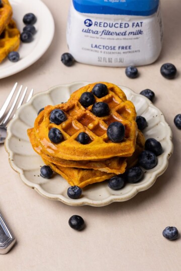 Heart-shaped pumpkin mochi waffles on a fluted white plate, next to a fork and a box of milk.