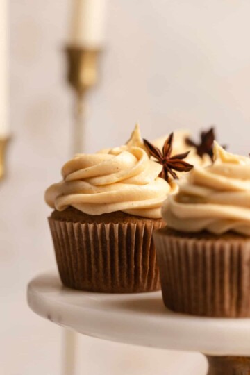 A pumpkin spice cupcake garnished with a star anise pod on a white marble cake stand.